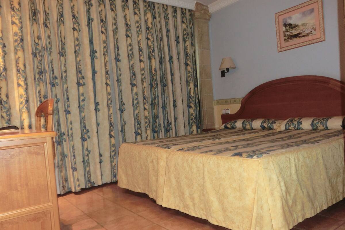Un dormitorio con una cama de madera, una mesita de noche, una lámpara y una cortina estampada.