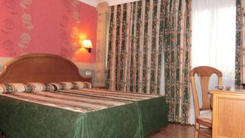 Habitación de hotel con cama, escritorio, silla, lámpara y cortinas.