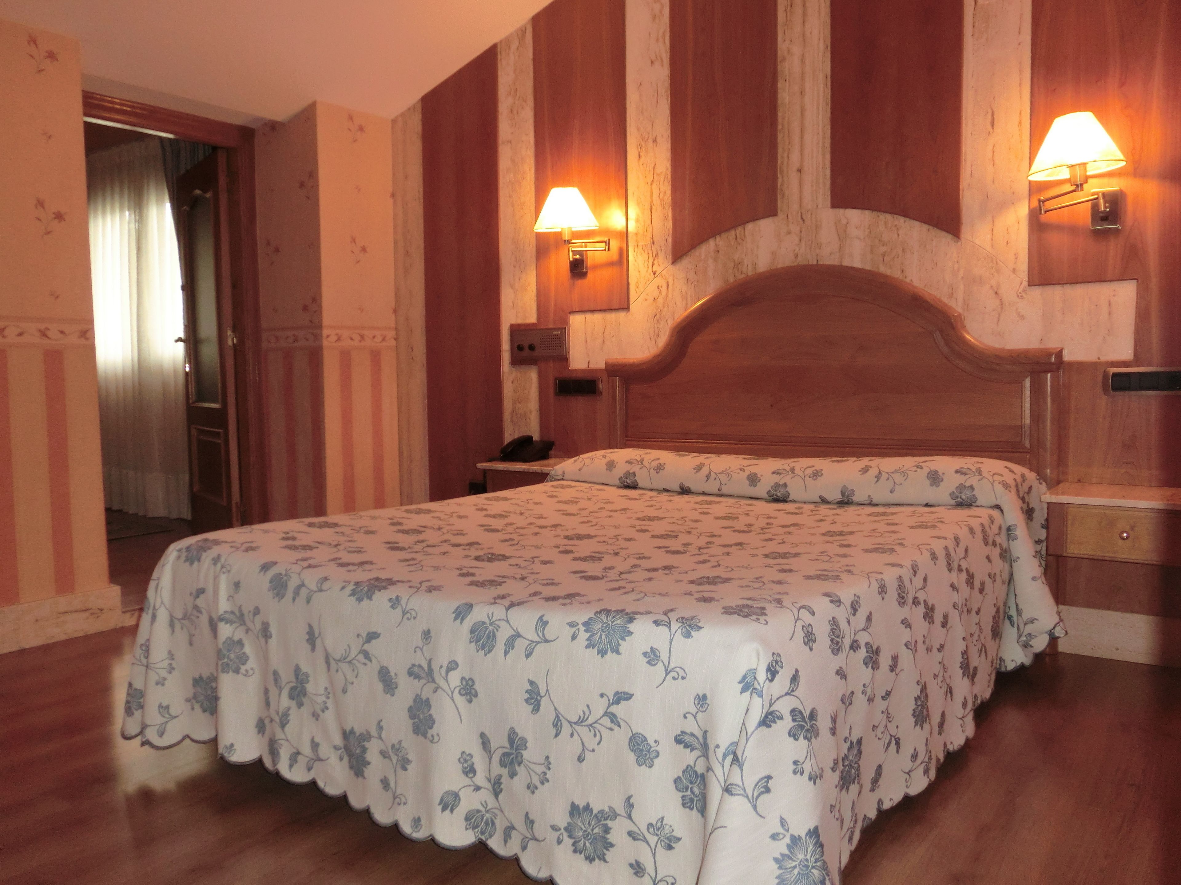 Ein Hotelzimmer mit einem hölzernen Kopfteil, einer blumigen Bettdecke, zwei Nachttischlampen und einem Nachttisch aus Holz.