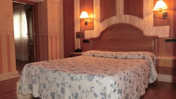Ein Hotelzimmer mit einem hölzernen Kopfteil, einer blumigen Bettdecke, zwei Nachttischlampen und einem Nachttisch aus Holz.