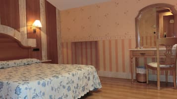A bedroom with a bed, a wooden desk, a chair, a mirror, and a wall with a floral pattern.