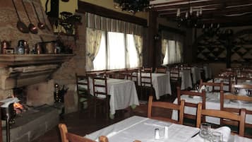 Una posada tradicional con paredes de piedra, muebles de madera y una chimenea. Las mesas están dispuestas con manteles blancos y sillas.