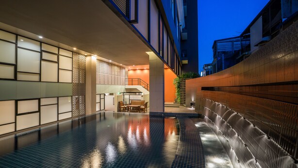 Une piscine intérieure moderne avec un sol carrelé, un espace détente avec une table et des chaises, et un escalier menant à un niveau supérieur.
