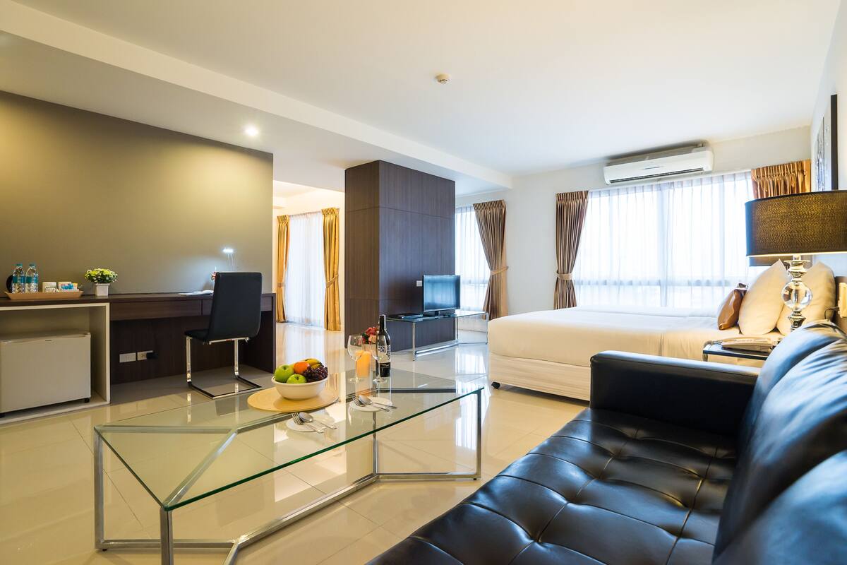 Een moderne hotelkamer met een glazen salontafel, een leren bank, een televisie en een eethoek met een kleine keuken.