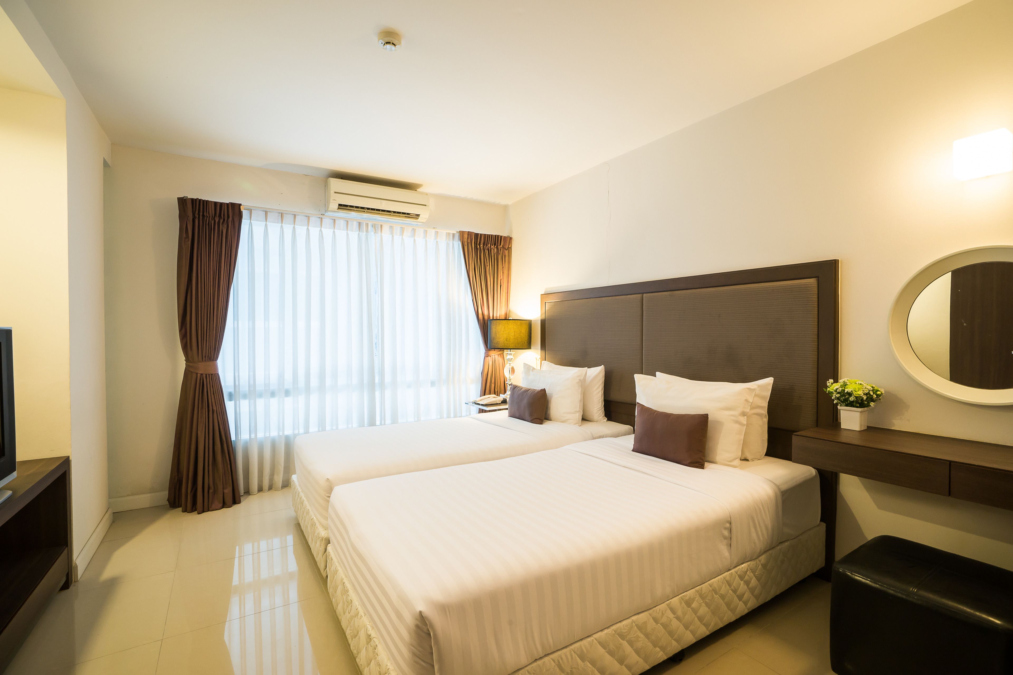 A hotel room with two beds, a large mirror, a bedside table with a lamp, and a TV.