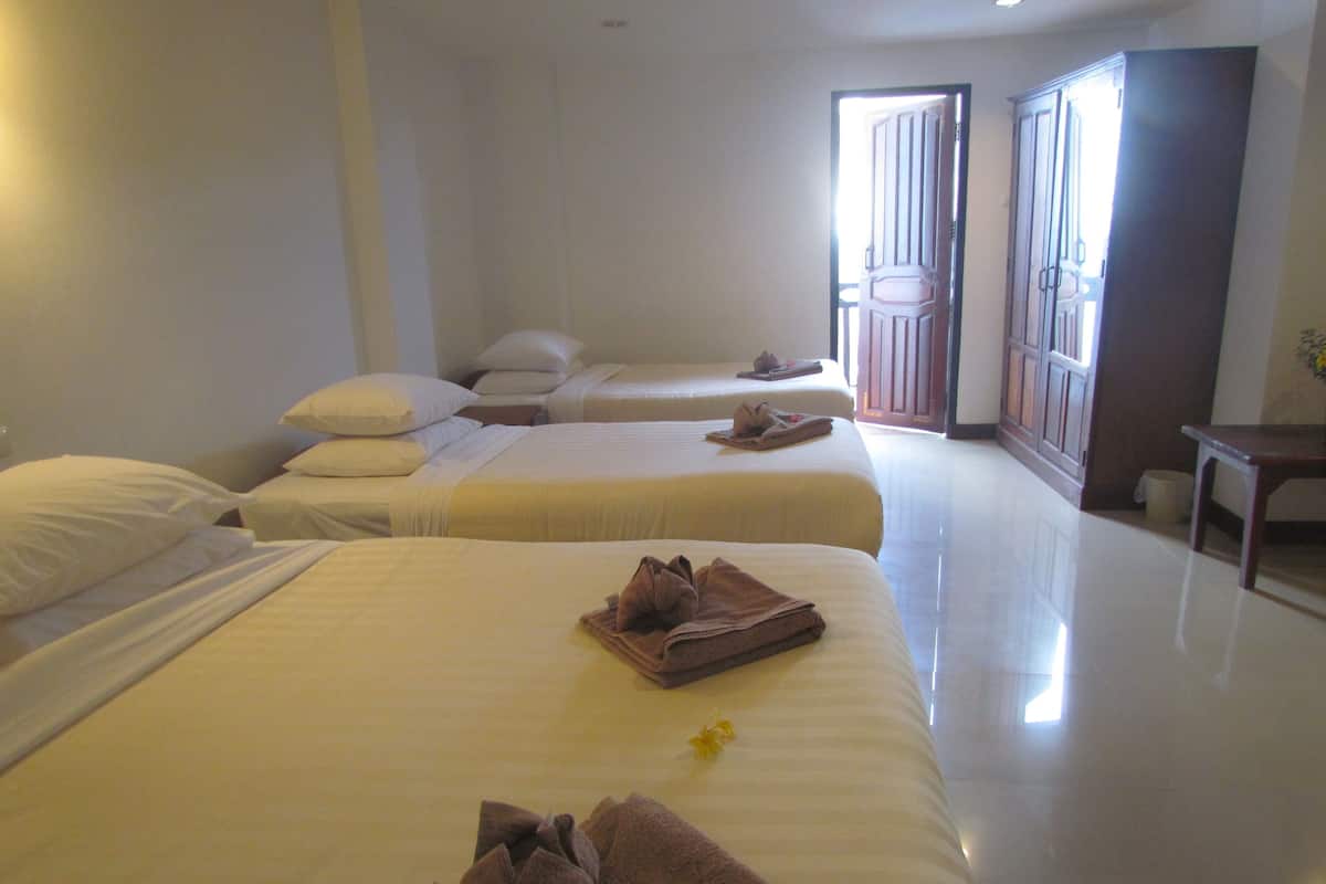 A hotel room with three beds, each with white linens and pillows. There is a wooden bench and a small table with a vase of flowers.