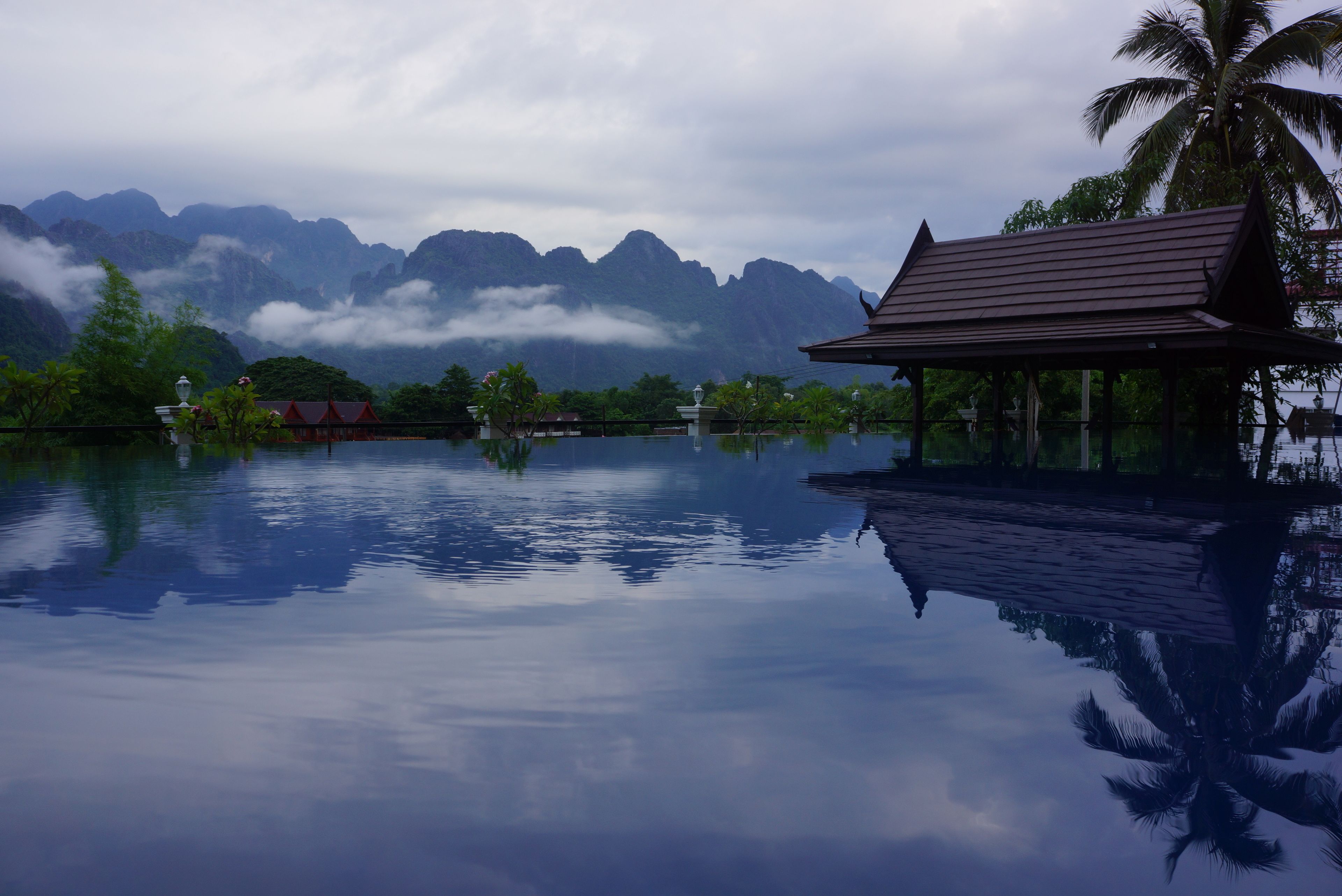 A serene water body reflecting a mountainous landscape with a traditional structure on the right.