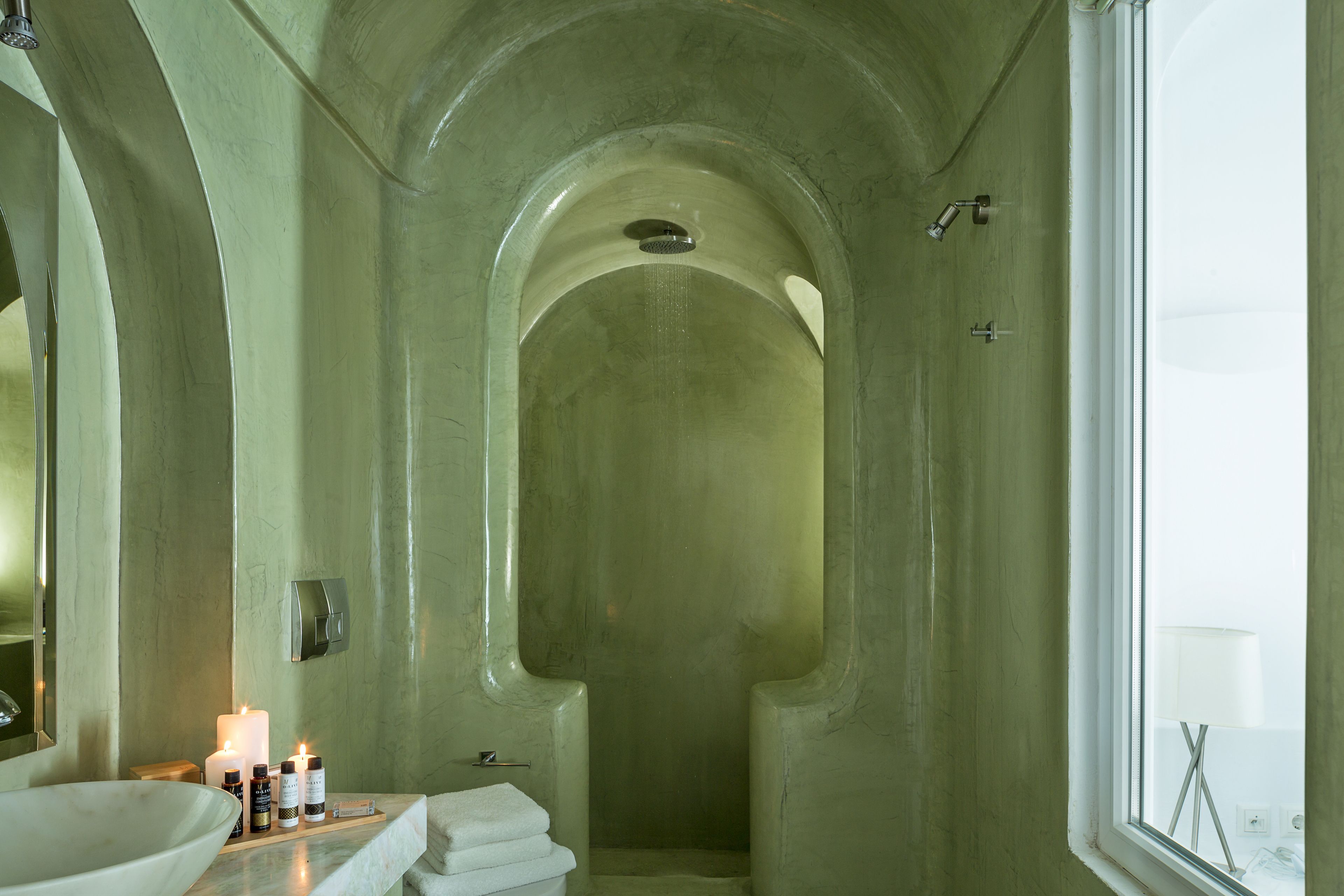 Un baño con una amplia ducha de arco, un lavamanos con artículos de aseo y una ventana que proporciona luz natural.