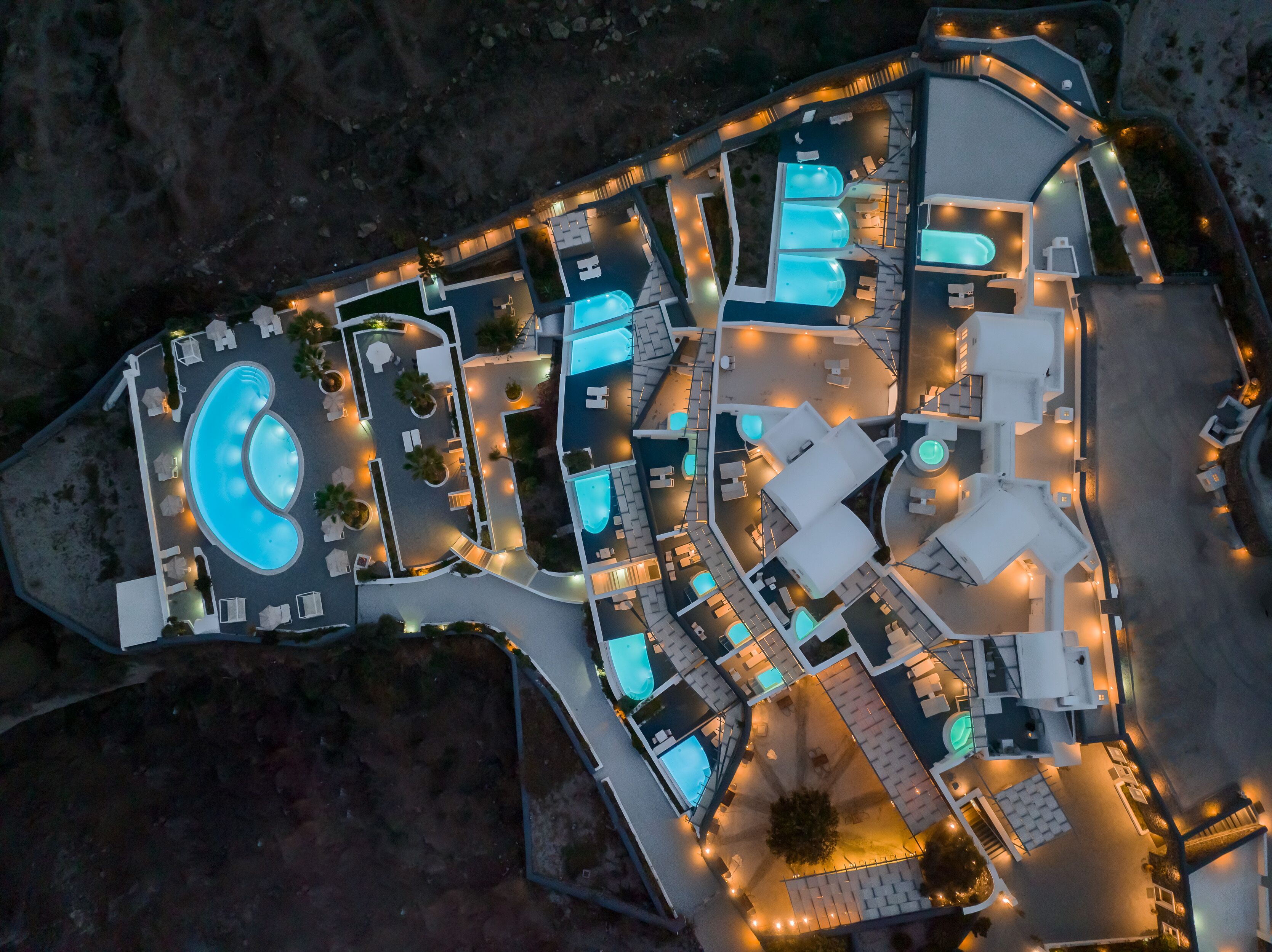 An aerial view of a resort with multiple swimming pools, outdoor seating areas, and well-lit pathways.