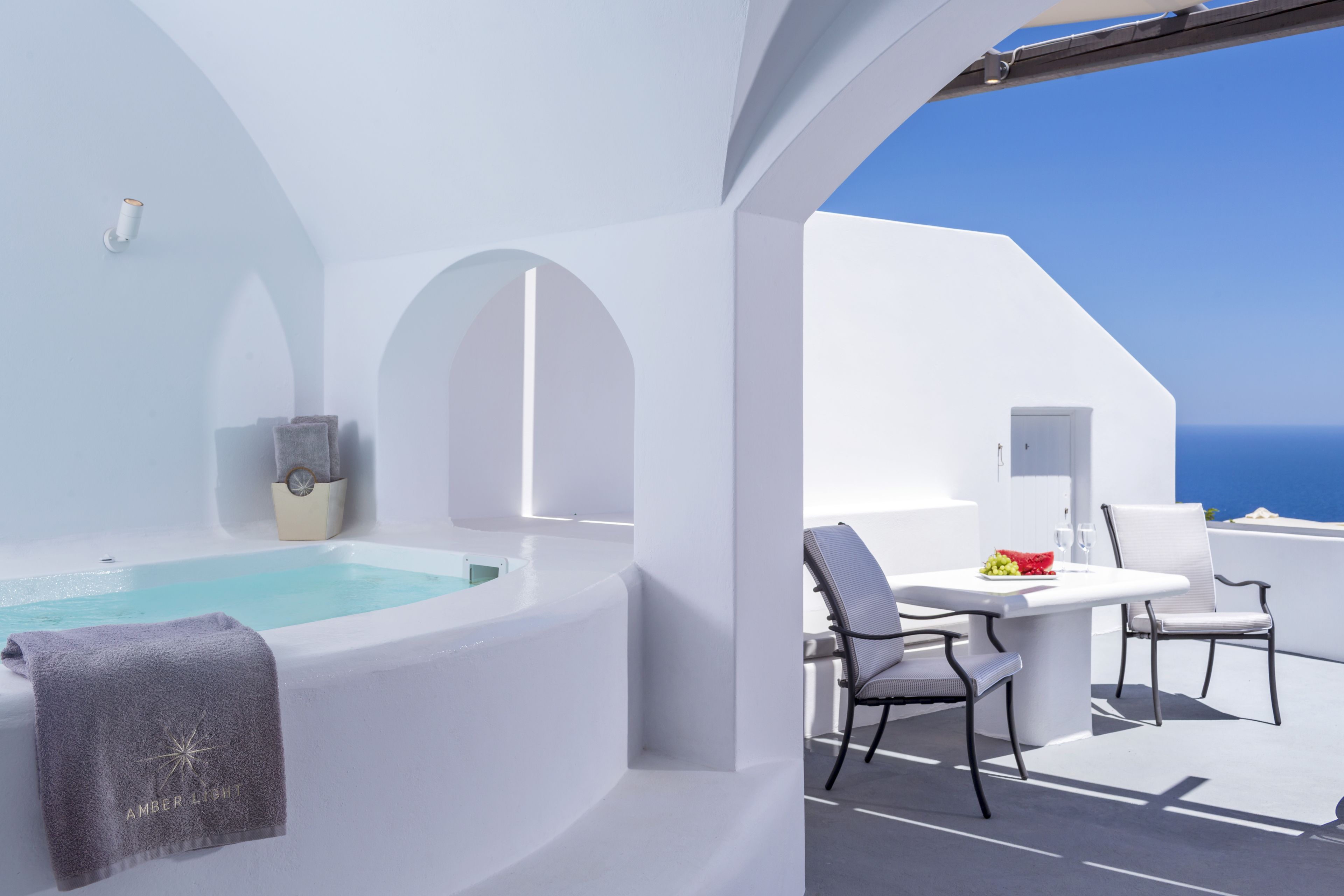 A white infinity pool with a towel, a table with chairs, and a view of the sea.