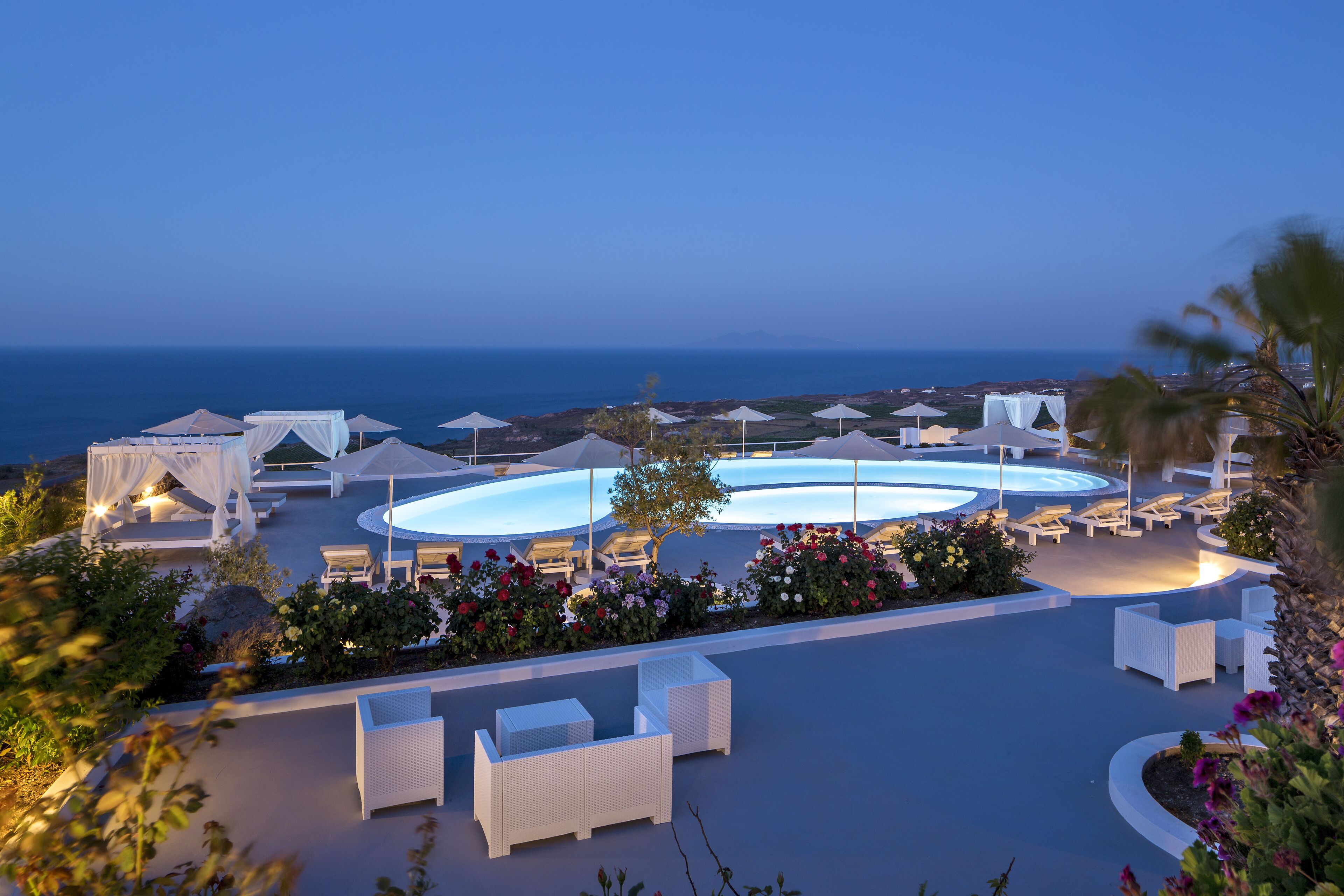 A resort with outdoor seating areas, a pool, and a view of the sea.