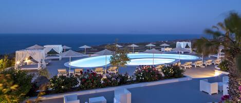 A resort with outdoor seating areas, a pool, and a view of the sea.