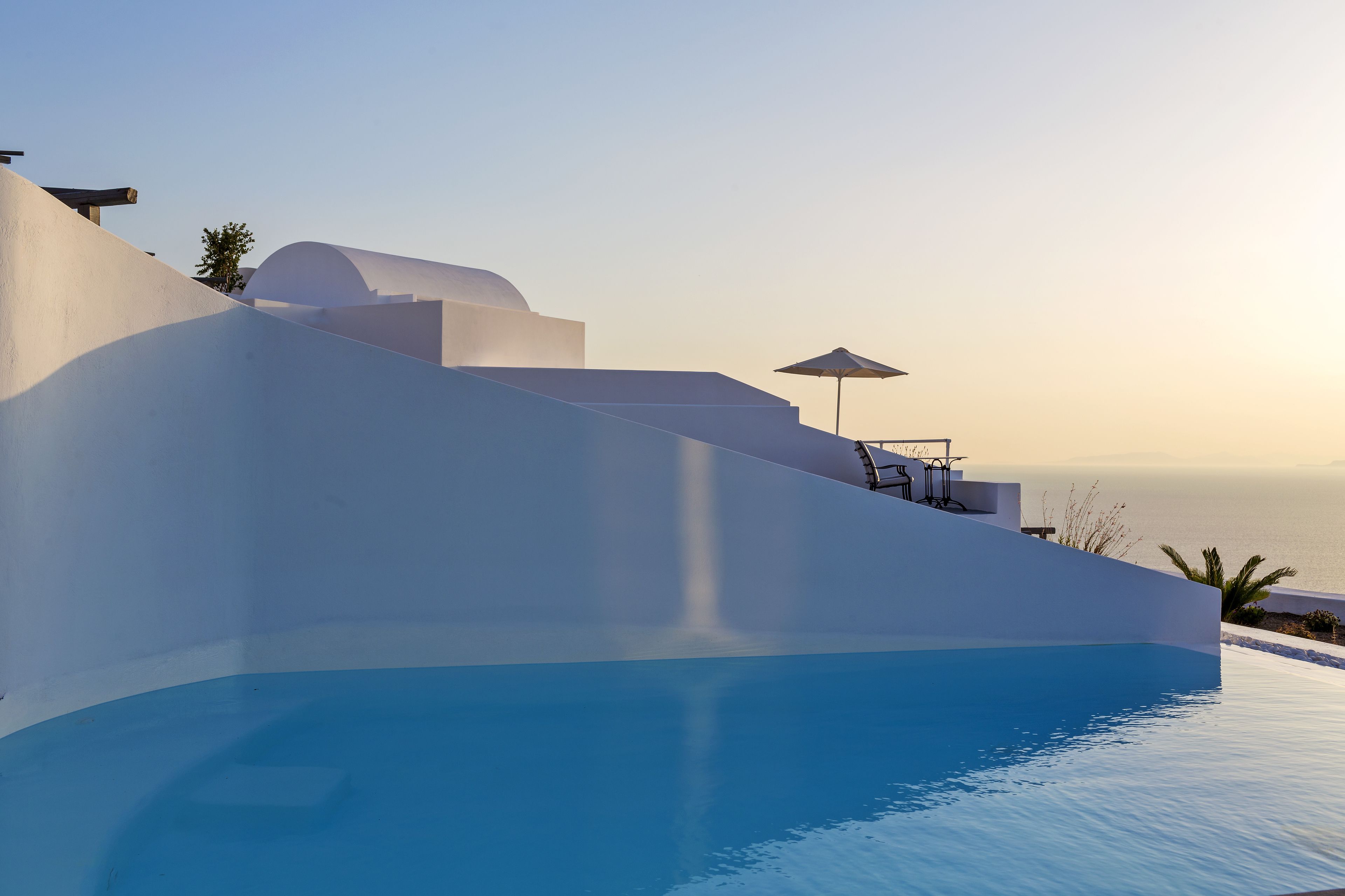 A modern building with a pool, white walls, and a view of the sea.