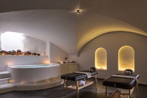 Et spa-rum med et stort badekar, to massagestole og et siddeområde med stearinlys.