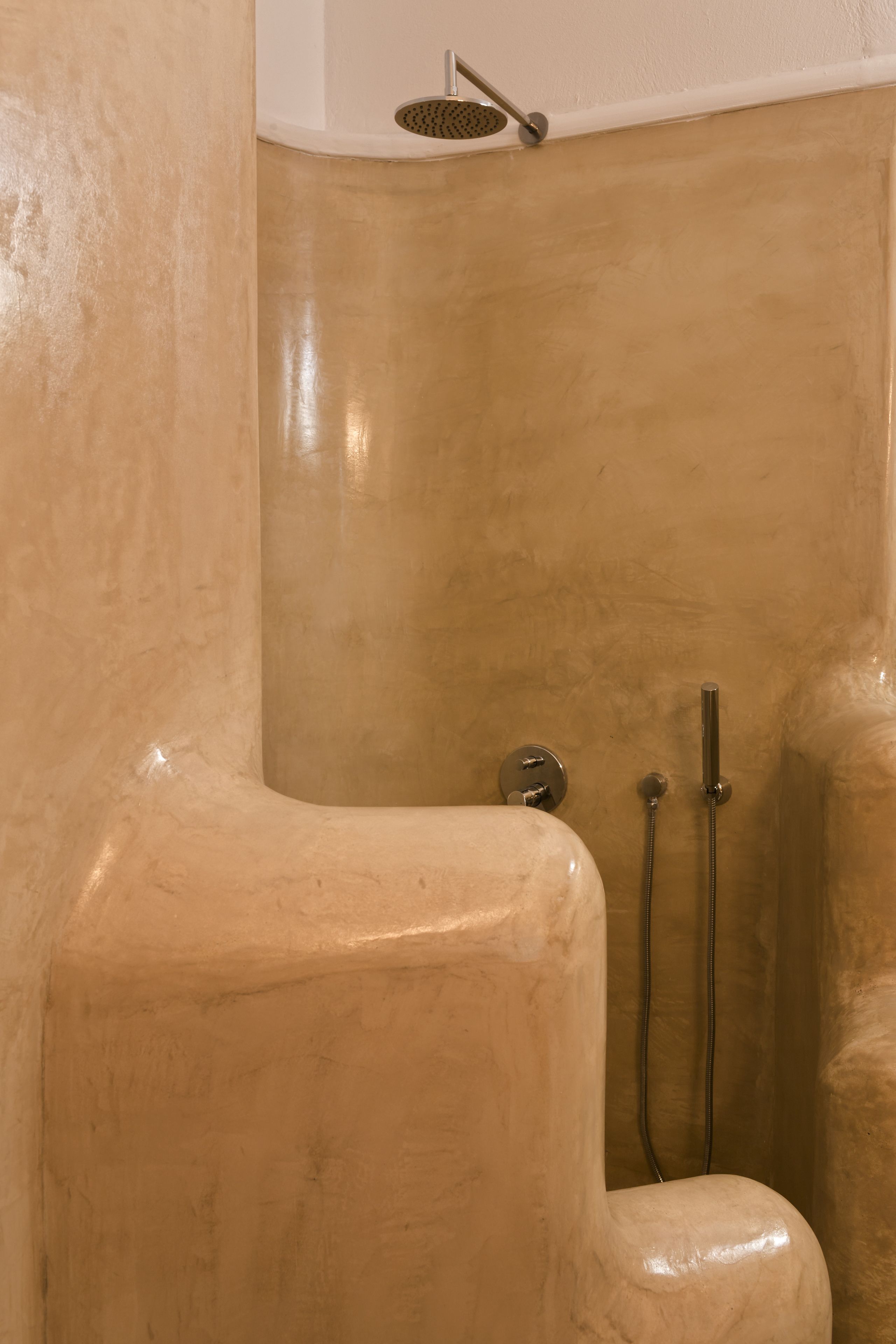 A bathroom with a beige tiled wall, a showerhead, and a handheld shower.