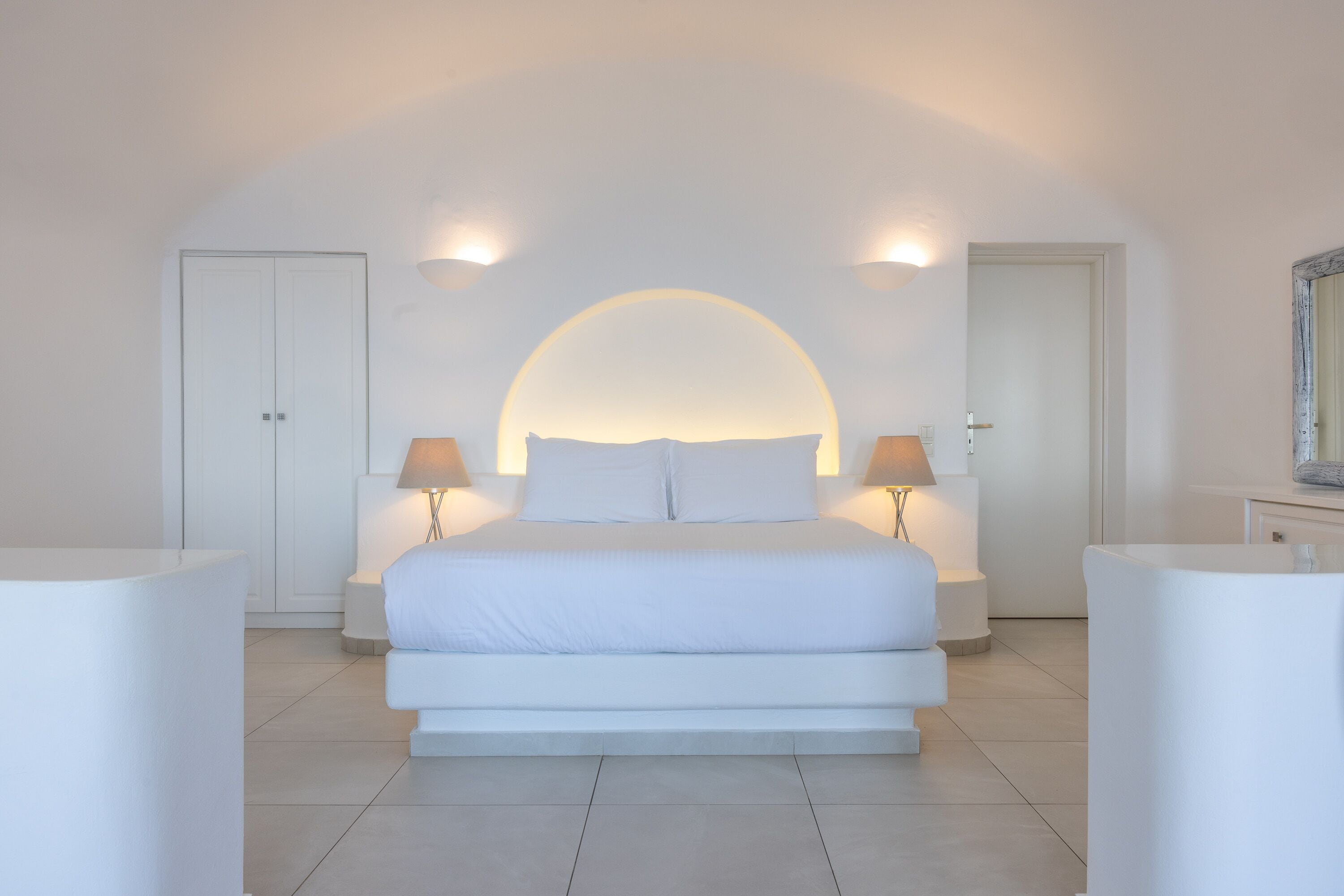 Une chambre moderne avec un grand lit, deux tables de chevet et un miroir au mur.