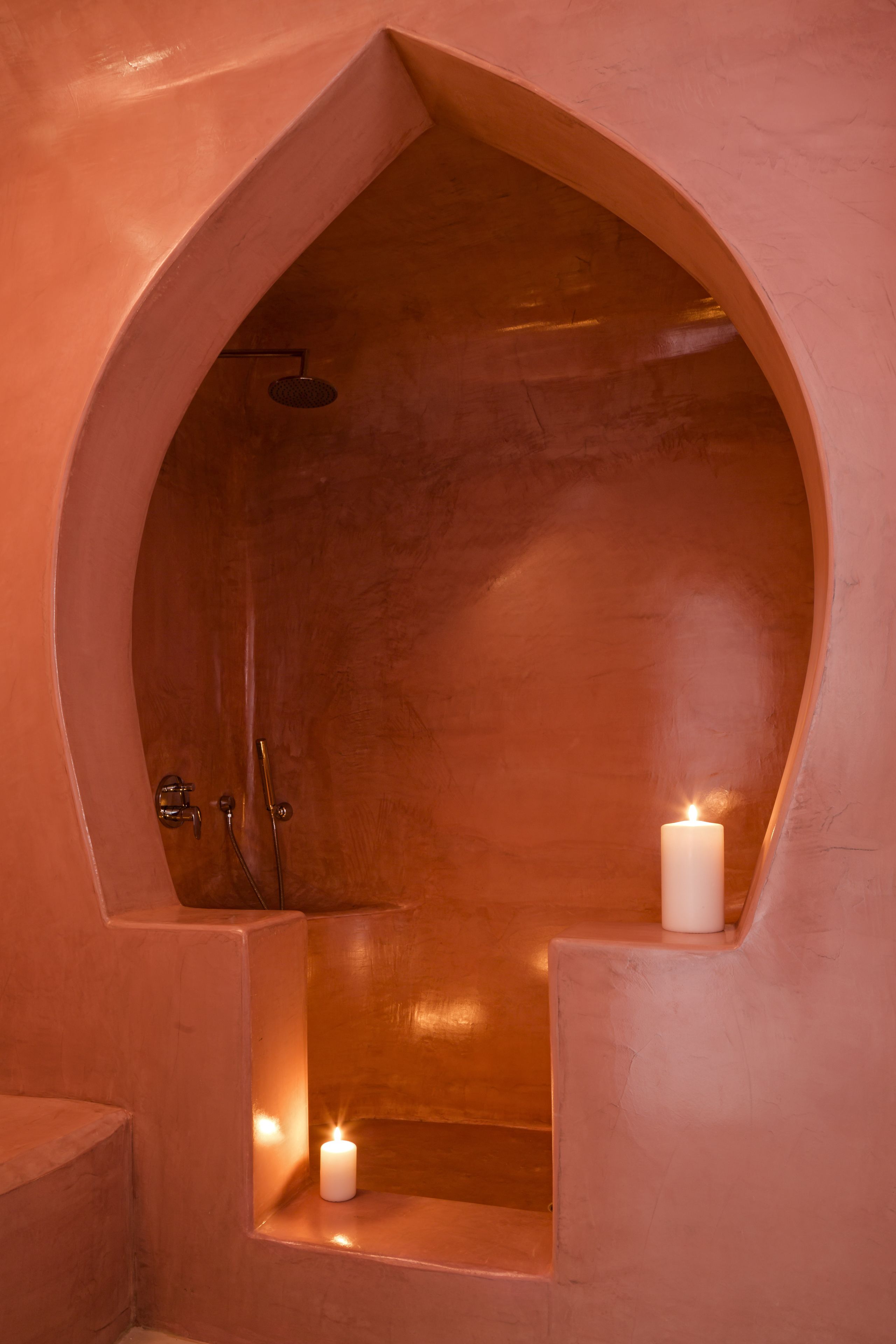 A bathroom with a large, arched bathtub, a showerhead, and two lit candles.