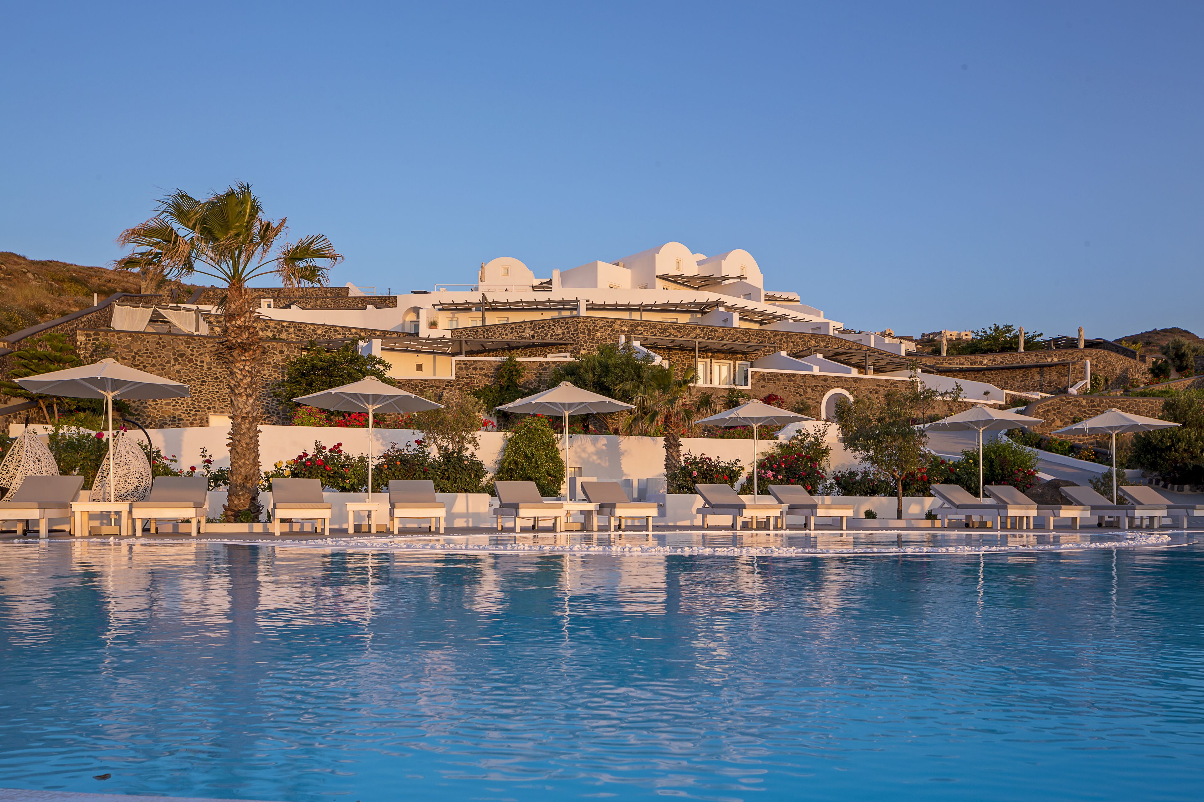 A resort with a pool, sun loungers, umbrellas, and a building with domed roofs.