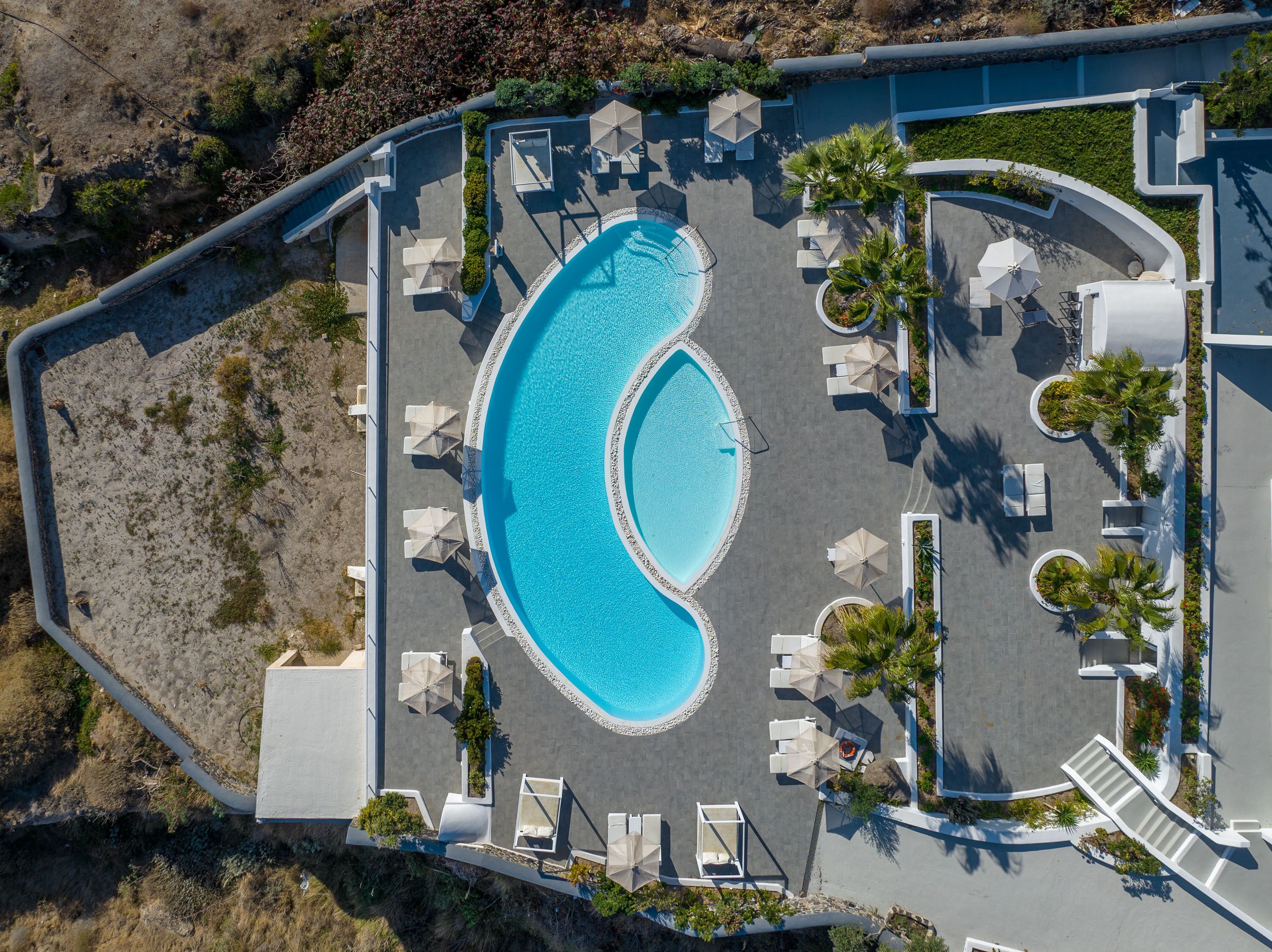 An aerial view of a resort with a large, crescent-shaped pool surrounded by lounge chairs and umbrellas.