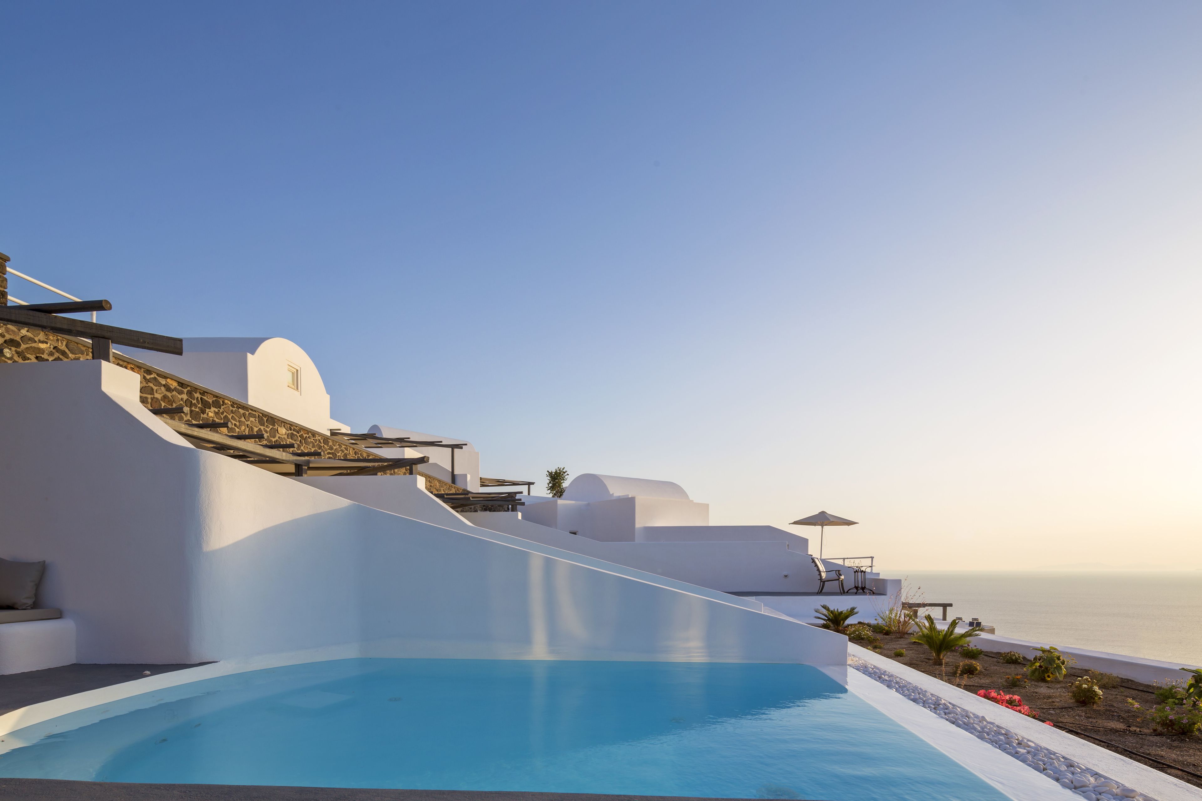 Un área de piscina moderna con vista despejada al mar, arquitectura blanca y mobiliario exterior.