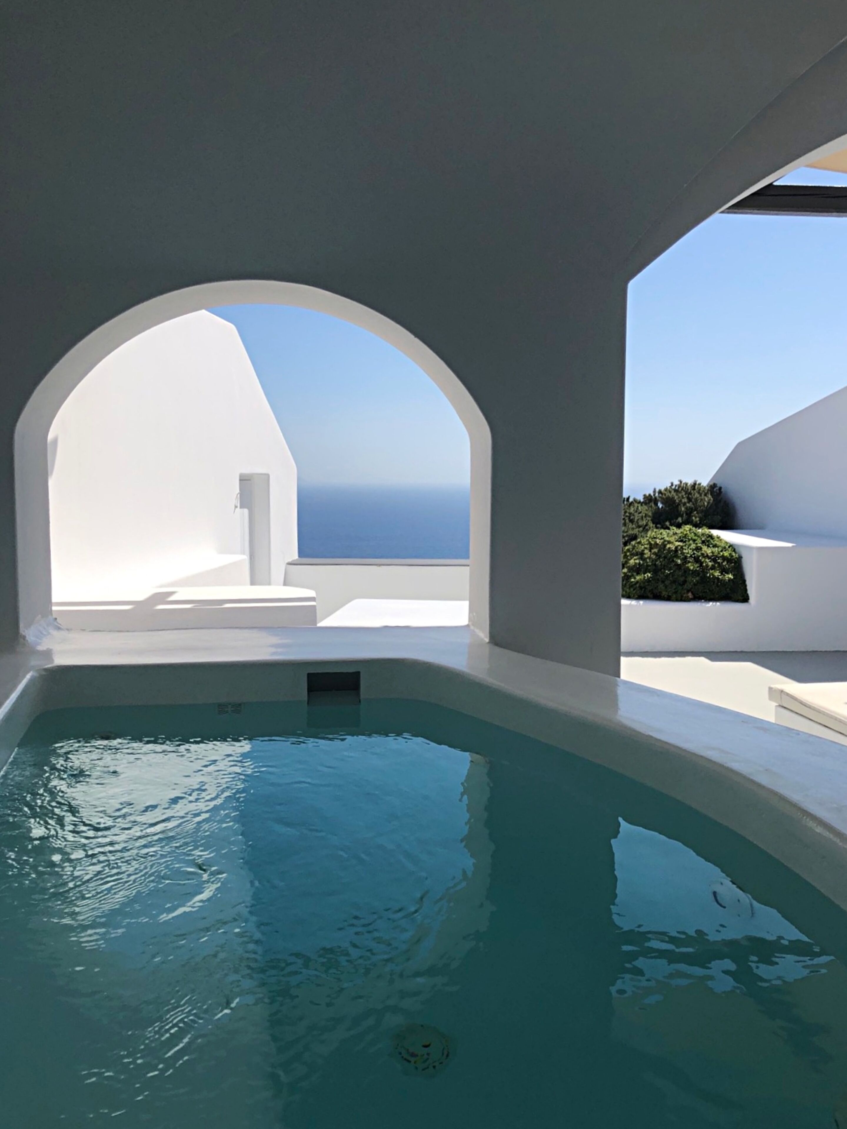Una piscina con vistas al mar, arquitectura blanca y un ventanal arqueado.