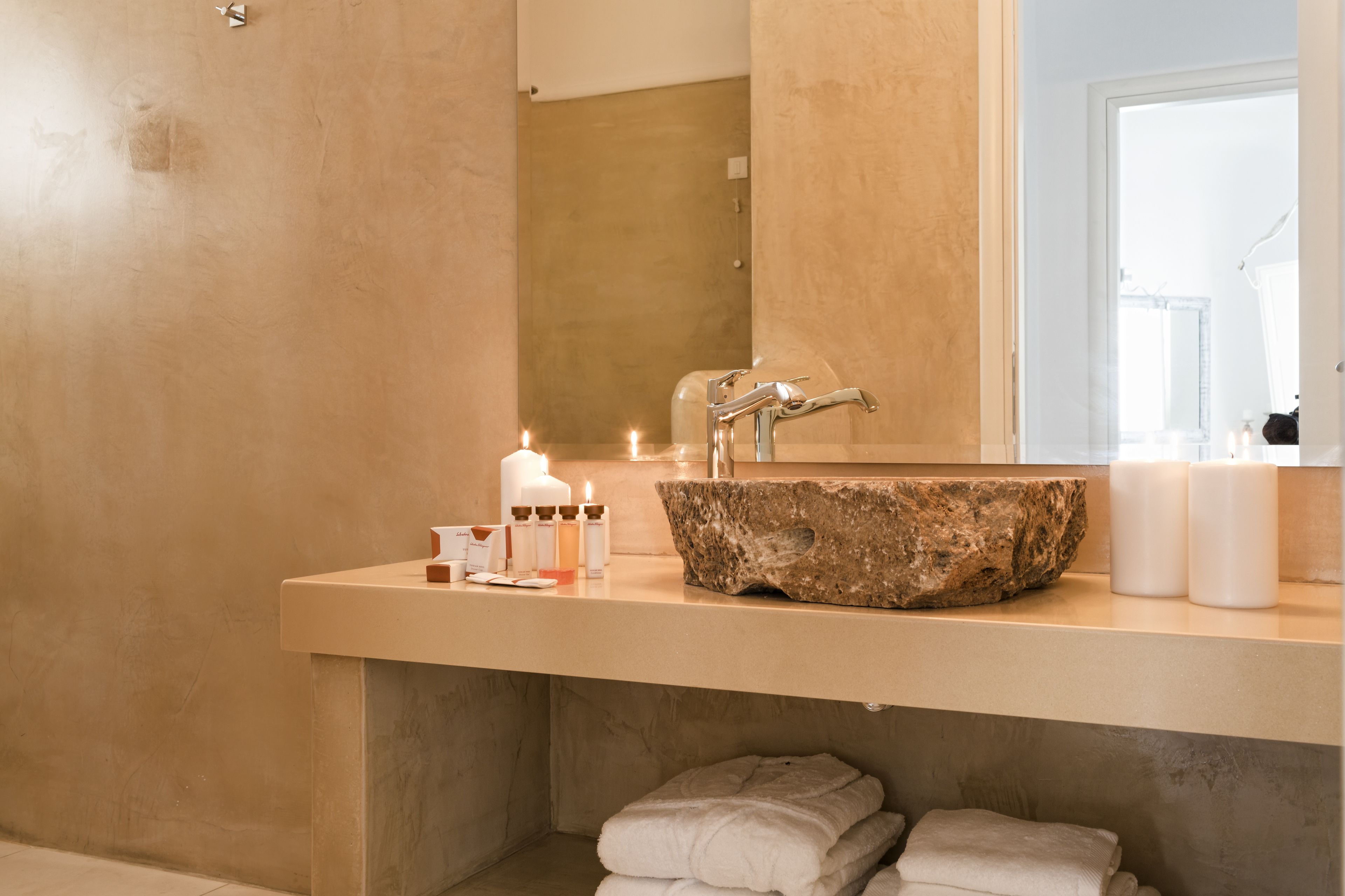 Ein Badezimmer mit einem Becken aus Stein, einem Spiegel und Kerzen.
