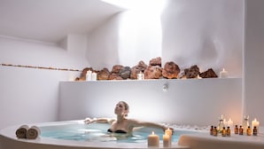 A woman relaxing in a bathtub with candles and bottles of essential oils.