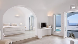 A modern bedroom with a bed, TV, and a balcony with a view of the sea.