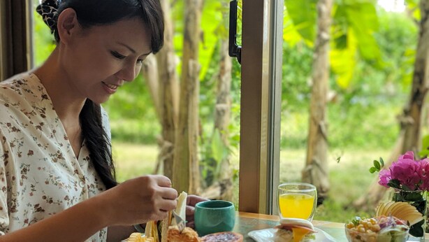 Eine Person sitzt an einem Tisch und speist von verschiedenen Gerichten, dazu steht ein Glas Orangensaft und eine Blumenvase.