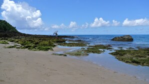 Ein Strand mit blauem Himmel, felsigen Abschnitten und ruhigem Wasser.