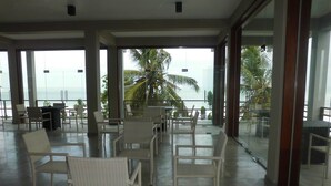 A spacious indoor area with multiple seating arrangements, large windows offering a view of palm trees and the sea. - Paradise Beach Club (Mirissa)