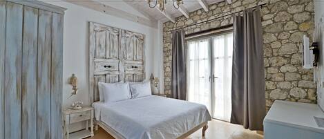 A bedroom with a stone wall, a bed, a nightstand, and a dresser.