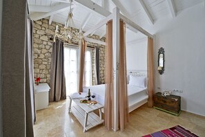 A bedroom with a stone wall, a bed with a canopy, a small table with a bottle of wine, and a dresser. - Bay C Hotel (Cesme)