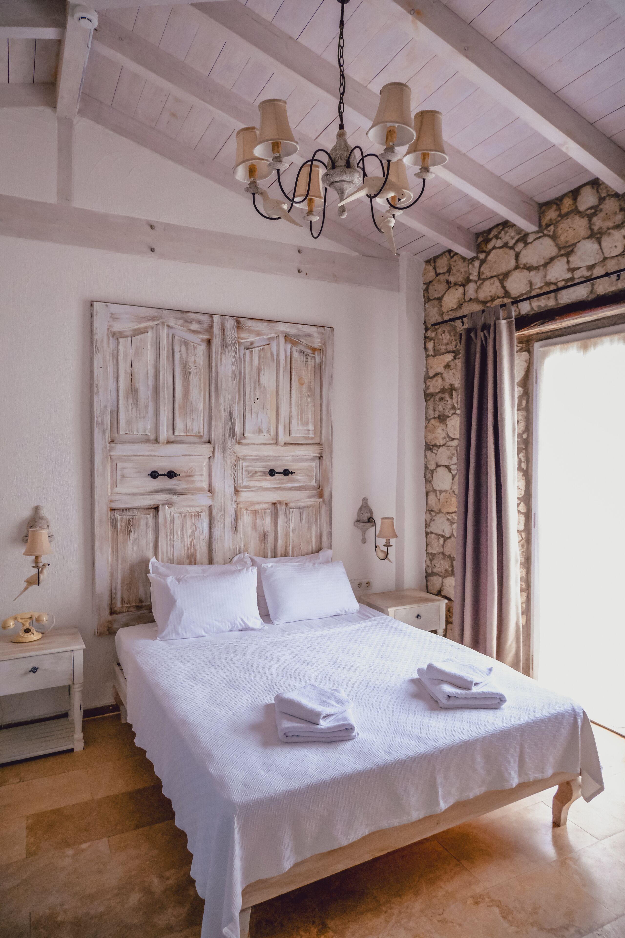 Un dormitorio con cama, mesita de noche, lámpara de pared y pared de piedra.