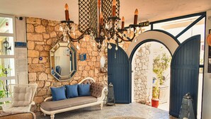 A cozy living area with a stone wall, a blue door, a sofa with blue cushions, a white chair, and a coffee table with a book. - Bay C Hotel (Cesme)