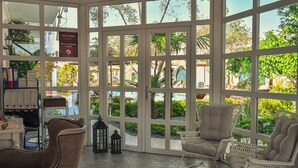 A room with large windows, wicker chairs, a small table, and a bookshelf. - Bay C Hotel (Cesme)