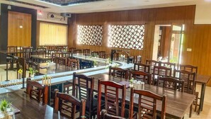 Un restaurant spacieux, doté de nombreuses tables et chaises, d’une allée centrale et d’un plafond orné de motifs.