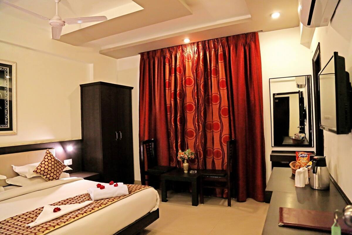 A hotel room with a bed, a desk, a chair, a wardrobe, a mirror, and a television.