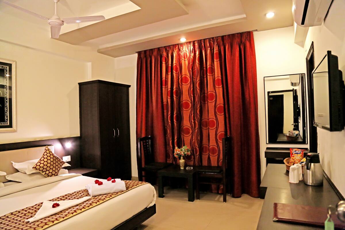 A hotel room with a bed, a desk, a chair, a wardrobe, a mirror, and a window with curtains.