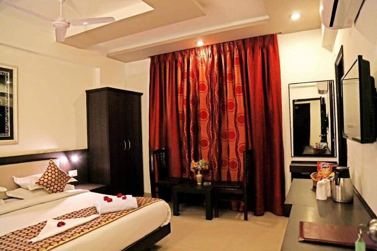 A hotel room with a bed, a desk, a wardrobe, a mirror, and a window with curtains.
