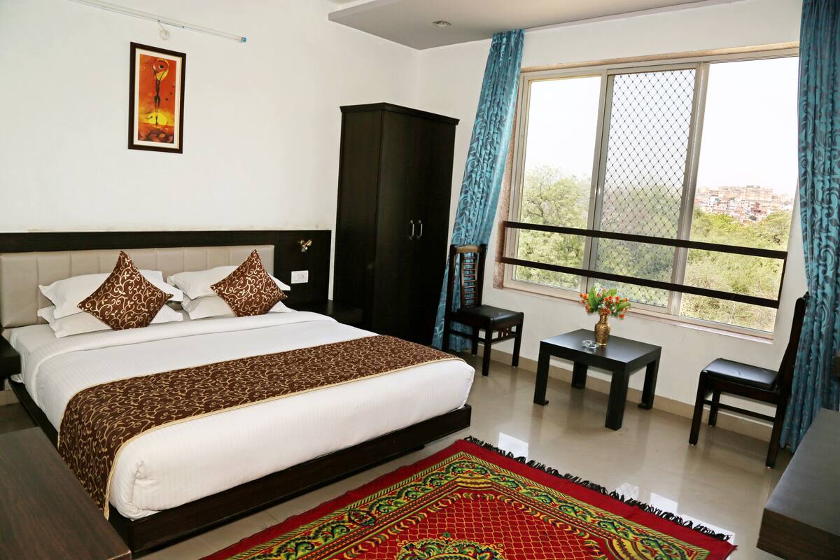 A hotel room with a large bed, a wardrobe, a small table with a vase, and a window with a view.
