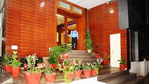 L’entrée d’un hôtel, avec un homme debout près de la porte, des plantes en pot et un escalier menant à l’intérieur.