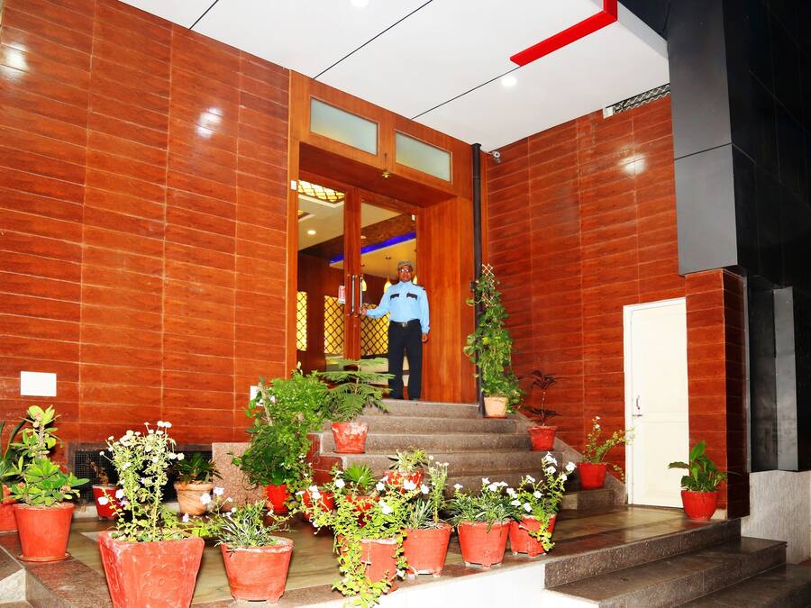 Entrada de un hotel con un hombre de pie en la puerta, plantas en macetas y una escalera que conduce al interior.