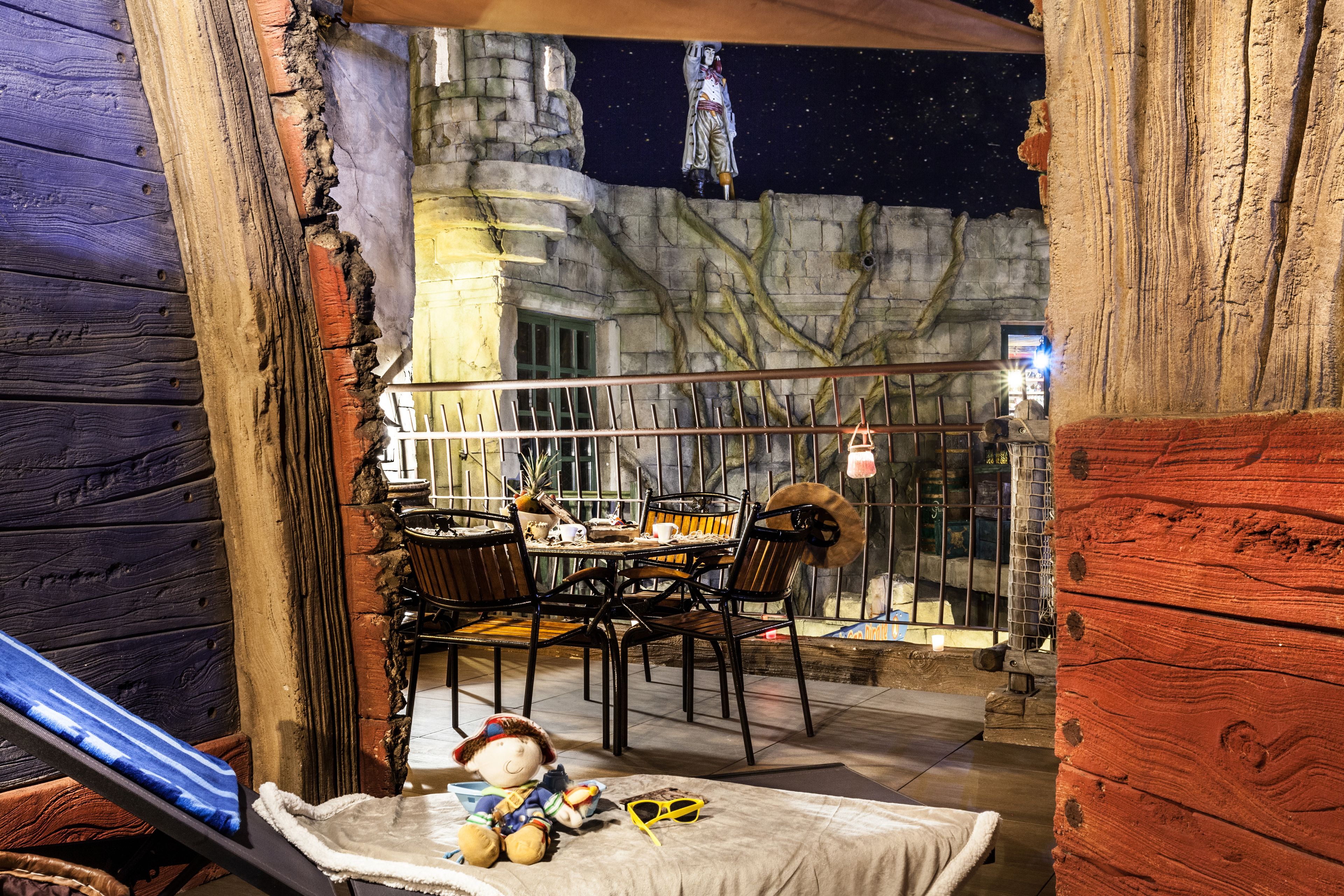A balcony with a dining table and chairs, a plush toy, and a pair of sunglasses on a cushion.