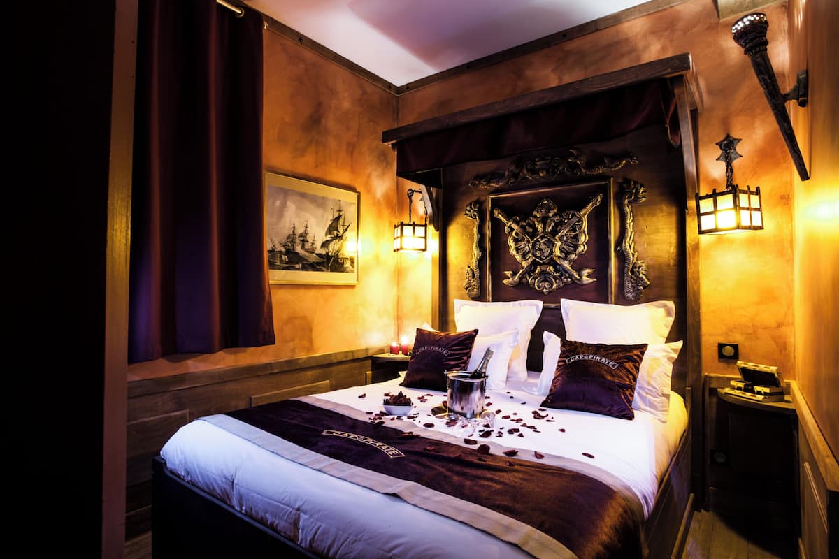 A bed with a decorative headboard, a nightstand with a lamp, and a framed picture on the wall.