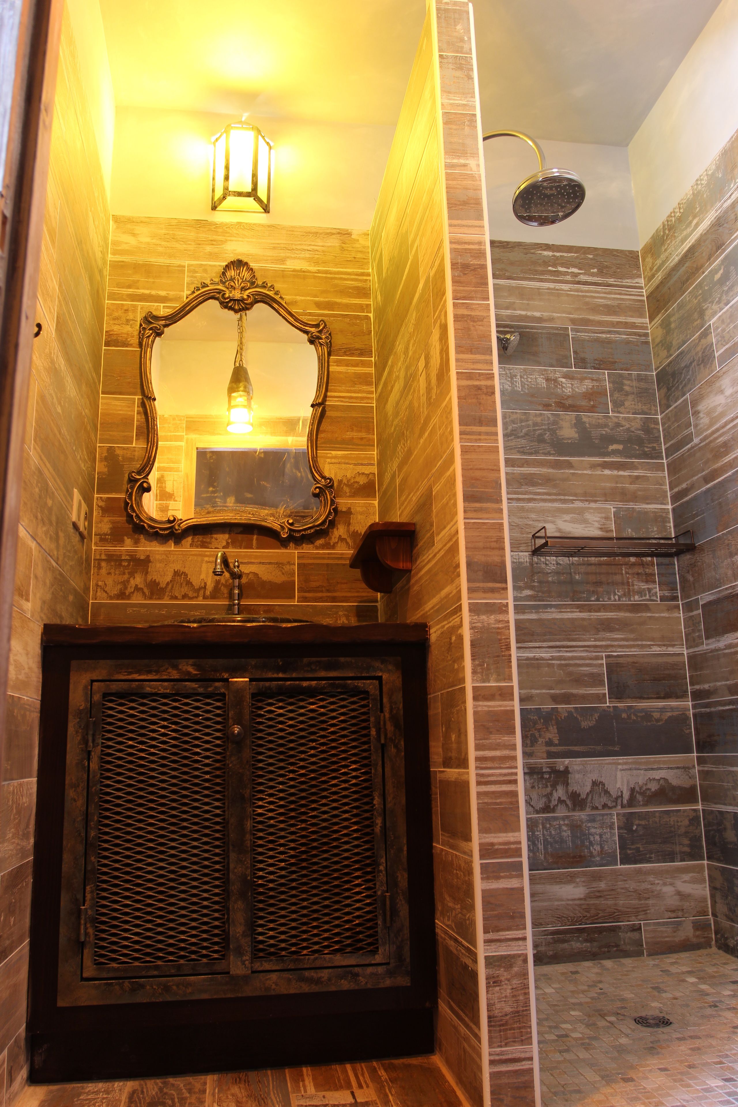 Un baño con tocador de madera, un espejo y zona de ducha con pared de azulejos.