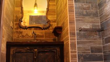 Un baño con tocador de madera, un espejo y zona de ducha con pared de azulejos.