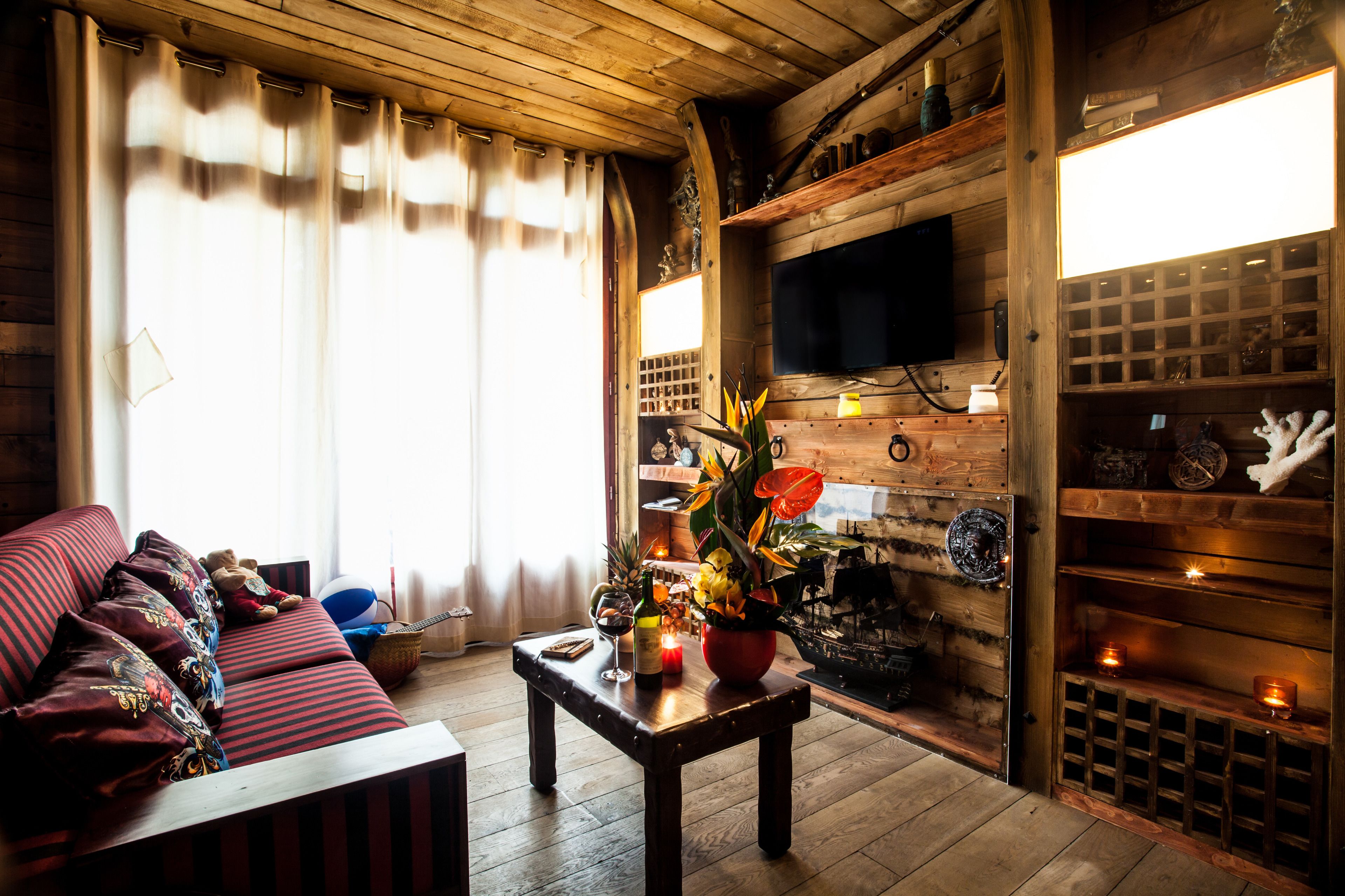 A cozy living room with a wooden ceiling, a sofa with patterned cushions, a coffee table with a vase and candles, and a fireplace with decorative items.