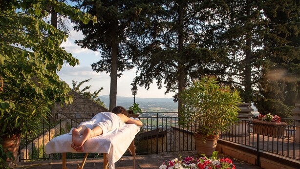 A person lying on a massage table outdoors with a view of mountains and trees.