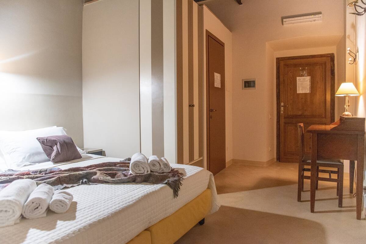 Een hotelkamer met een bed, een bureau en een stoel. Er liggen handdoeken op het bed en een lamp op het bureau.